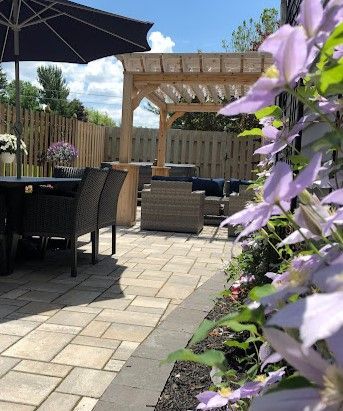 Illuminated backyard at dusk, featuring landscaping, decorative lights, and a white fence.
