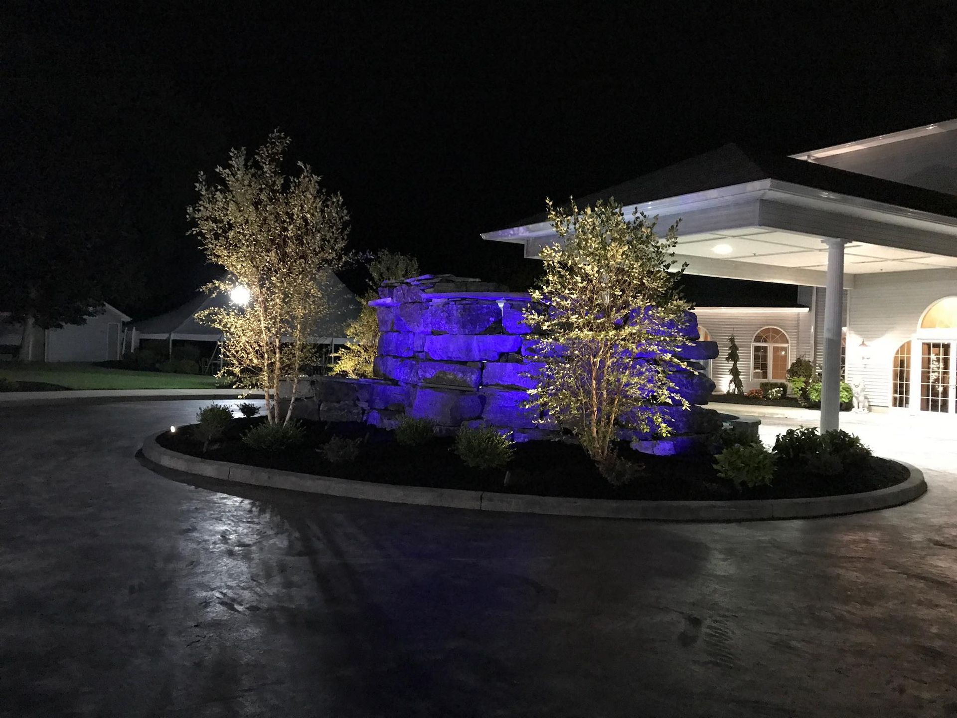 Lit-up rock waterfall and trees with string lights at night; building entrance visible.