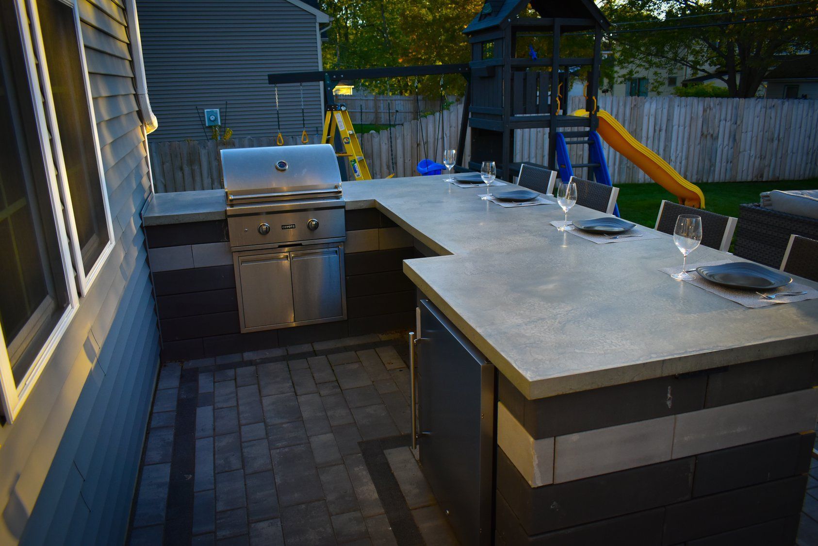 Outdoor kitchen with grill and countertop seating area; patio, playground in background.