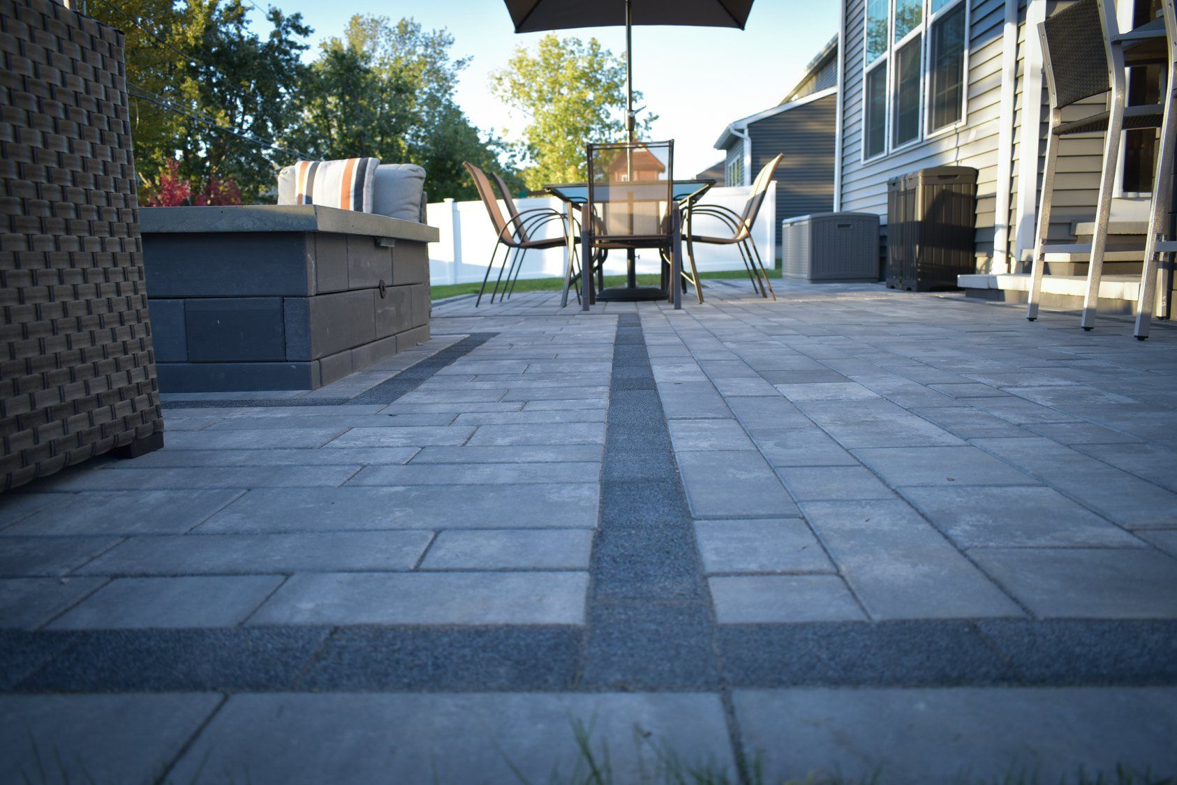 Patio with grey pavers, a table and chairs under an umbrella, and a fire pit.