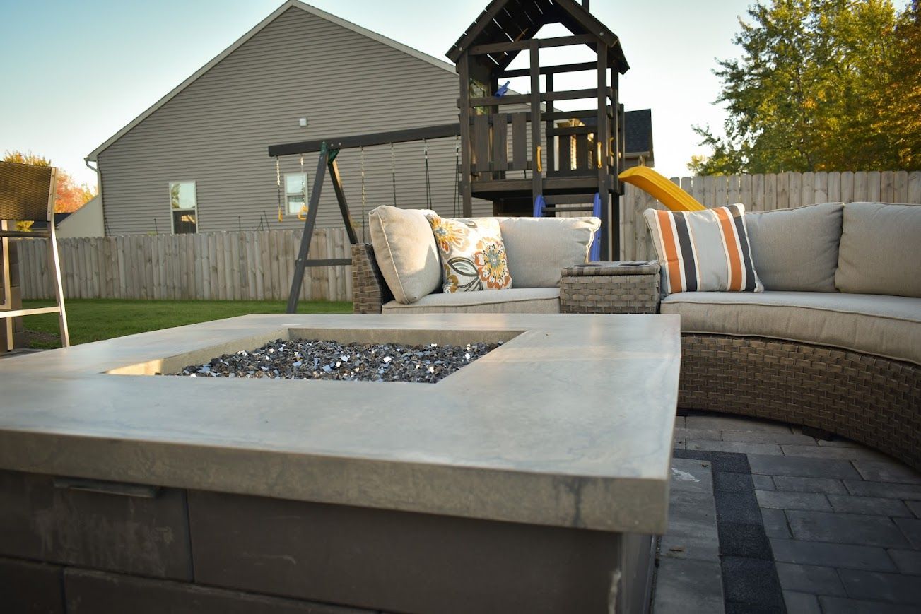 Outdoor patio with a fire pit, curved sofa, and a playset in the background.