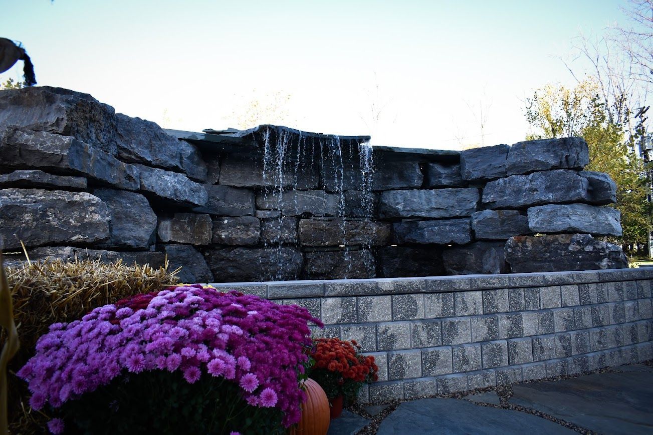 Stone waterfall with purple and orange mums in front.