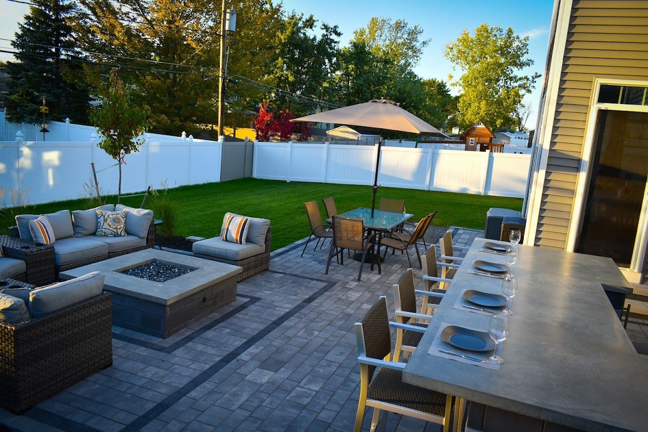 Patio with outdoor furniture, fire pit, dining area, and green lawn enclosed by a white fence.