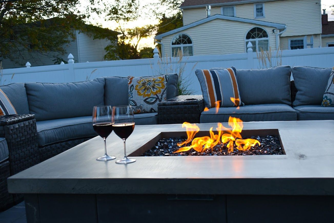 Outdoor patio with fire pit, seating, and wine glasses at dusk.