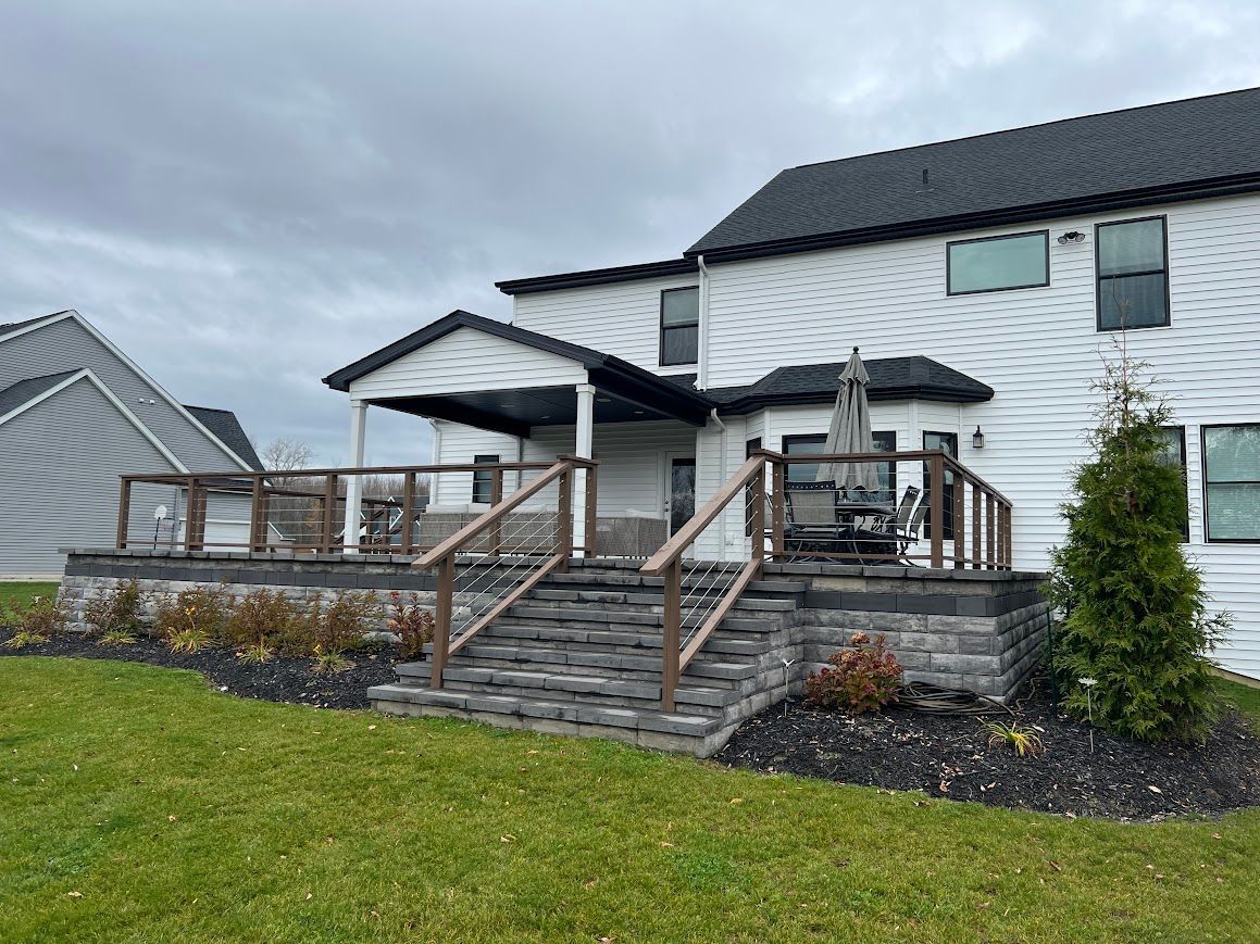 A two-story white house with a multi-level deck, a covered patio, and steps leading to a lawn.