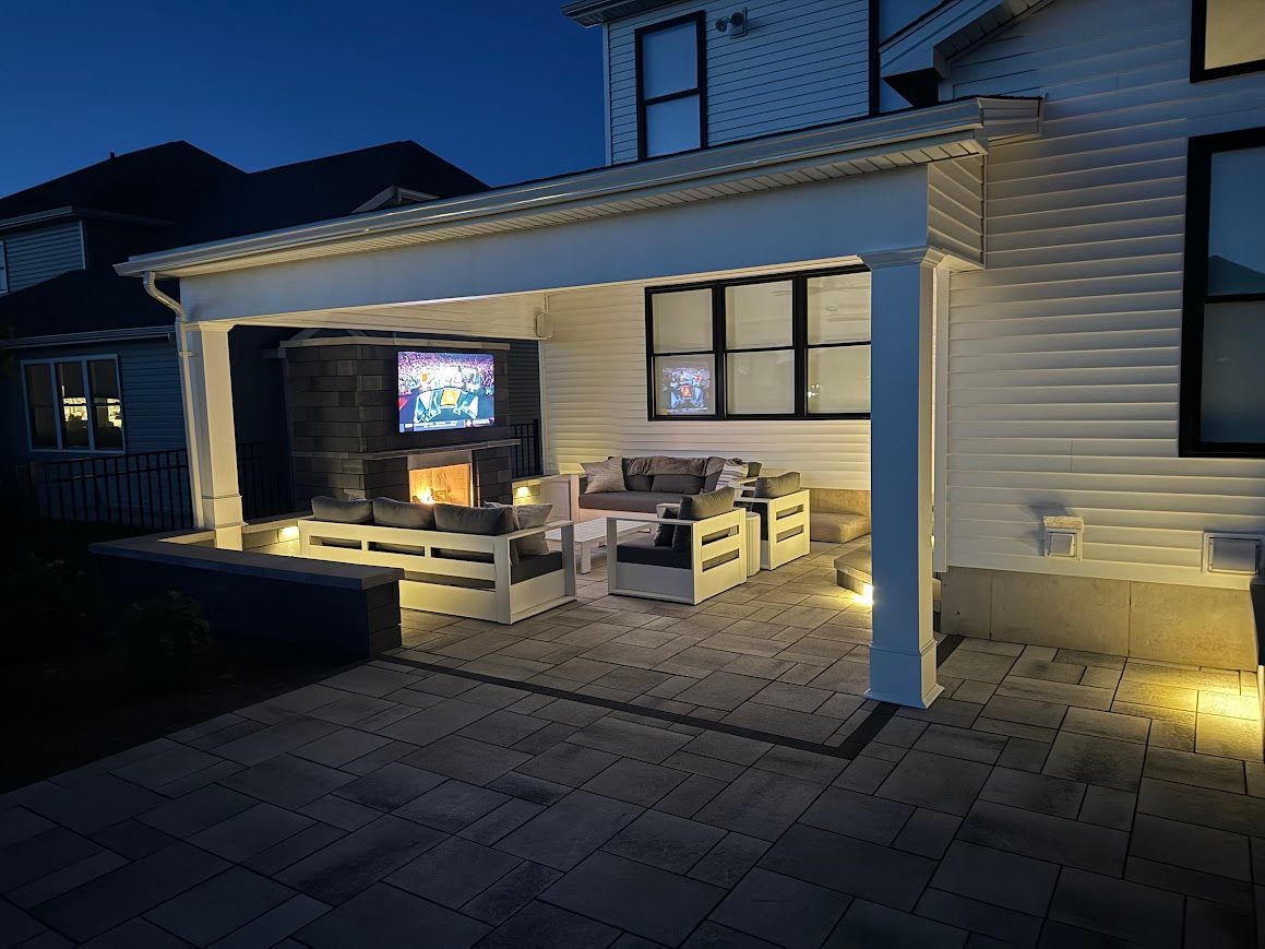 Outdoor patio with white pergola, seating, fireplace, and TV at night.
