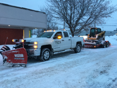 Orange snowplow clearing a snow-covered road in a forest.