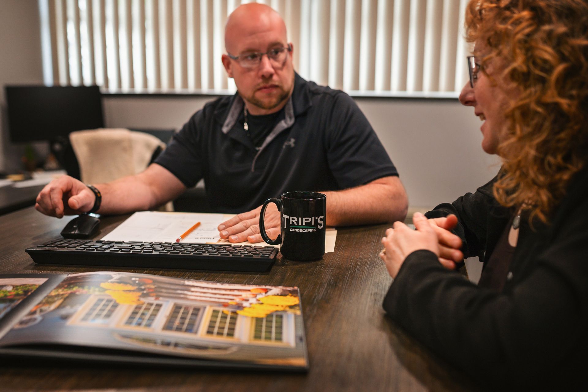 Man and woman seated at a desk, reviewing paperwork and a brochure. The man has a mug that says