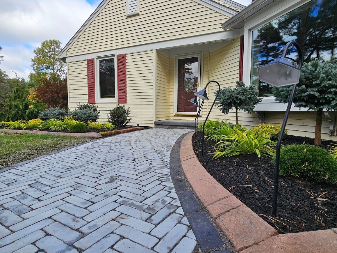 Paved walkway leading to a yellow house with red door and landscaping.