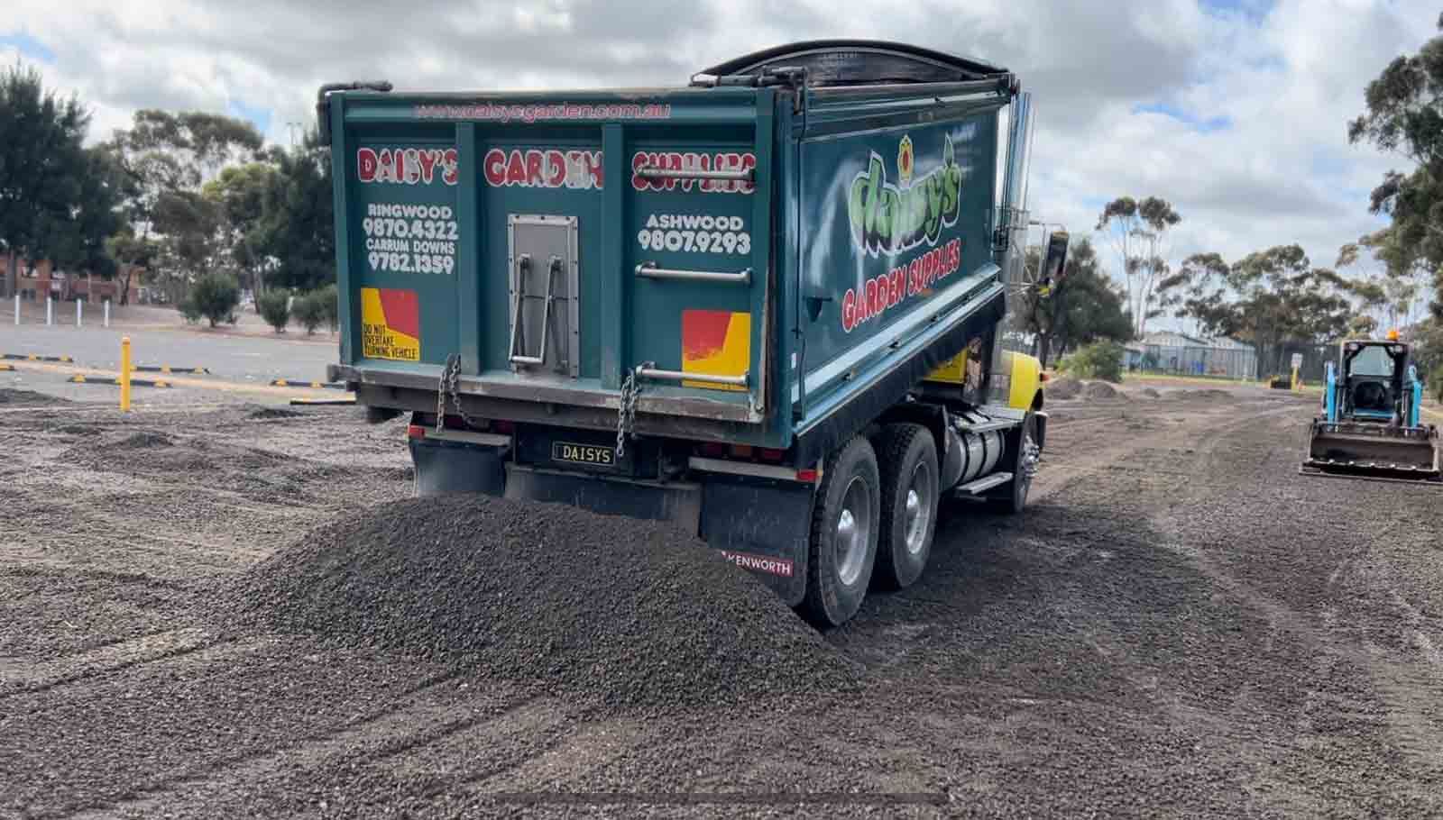 A dump truck is driving down a dirt road next to a bulldozer