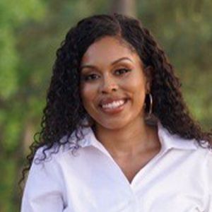 A woman with curly hair is wearing a white shirt and smiling.