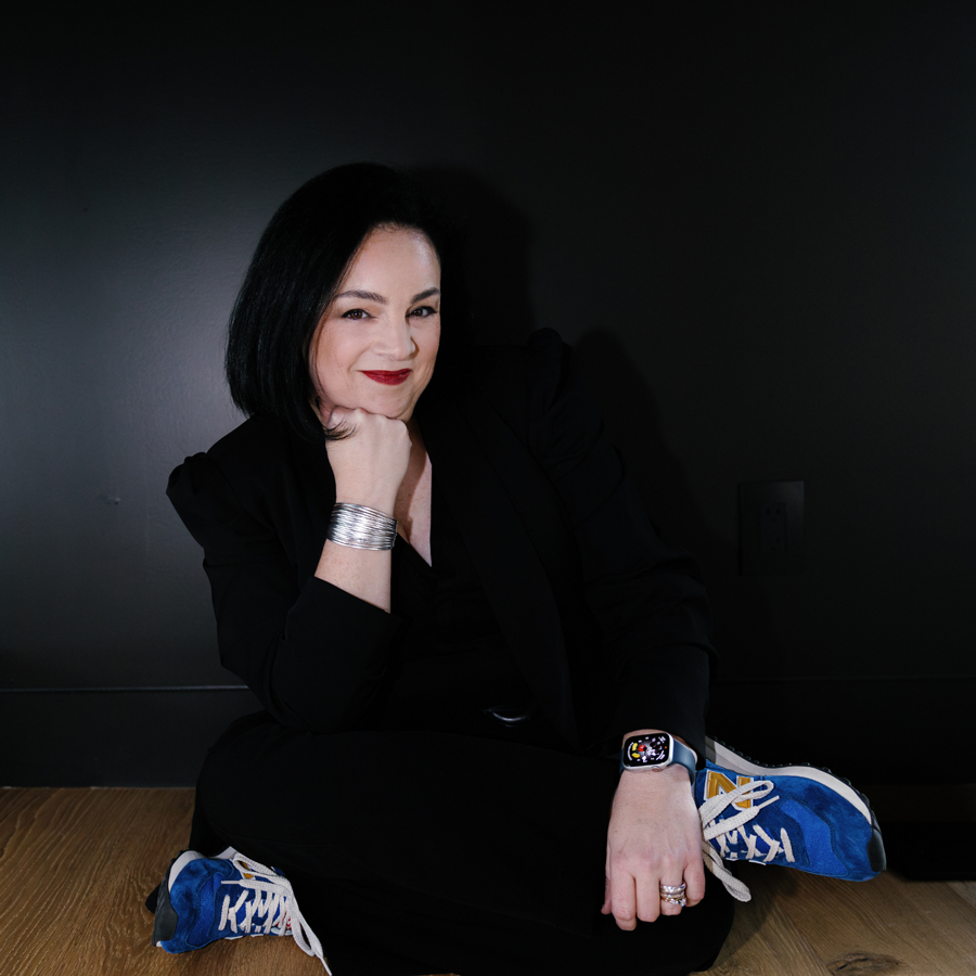 A woman is sitting on the floor wearing a watch and sneakers.