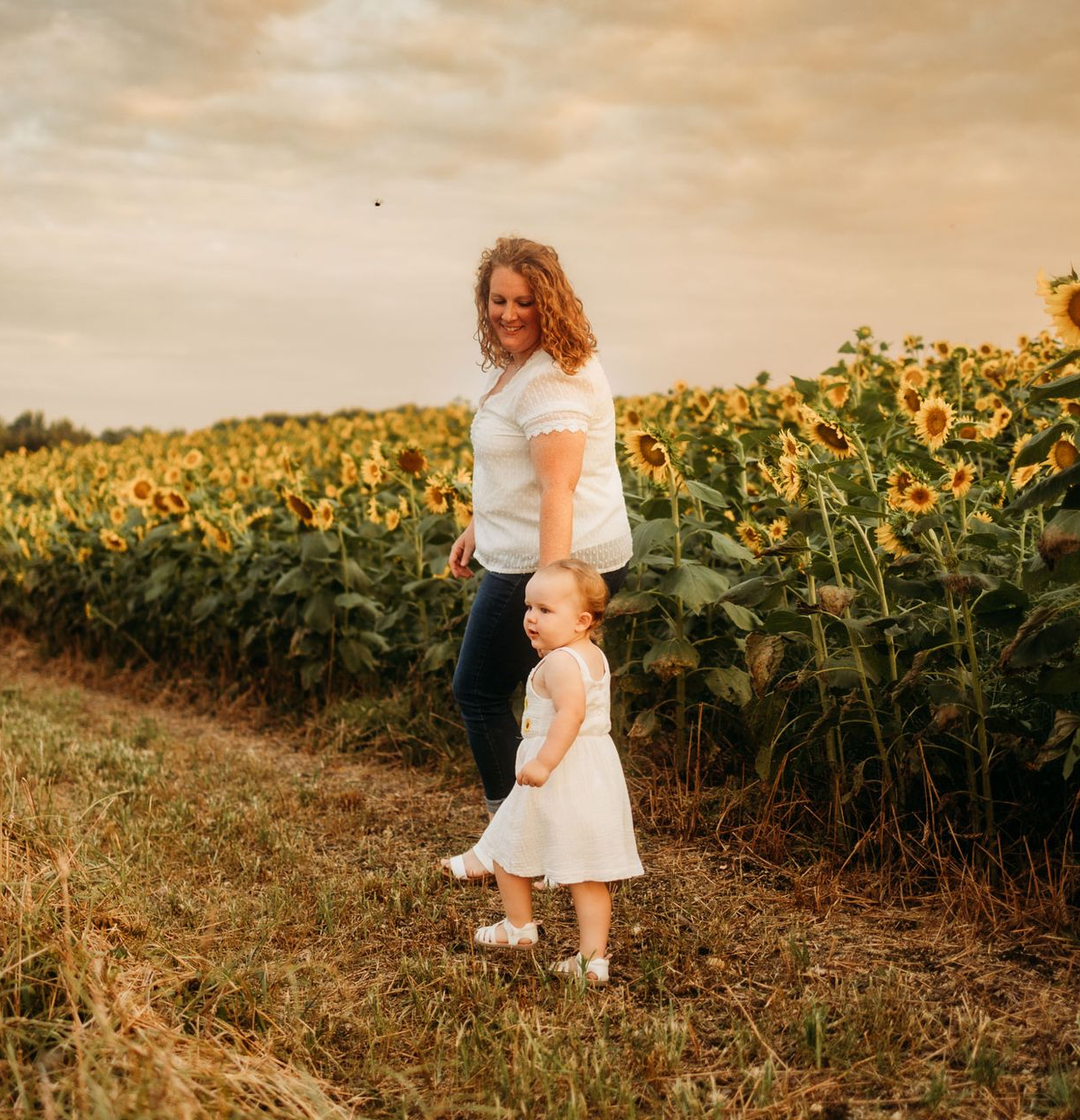 Woman and child standing in a sunflower field at sunset