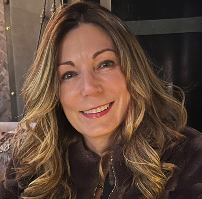 A woman with long hair is smiling and wearing a brown jacket.
