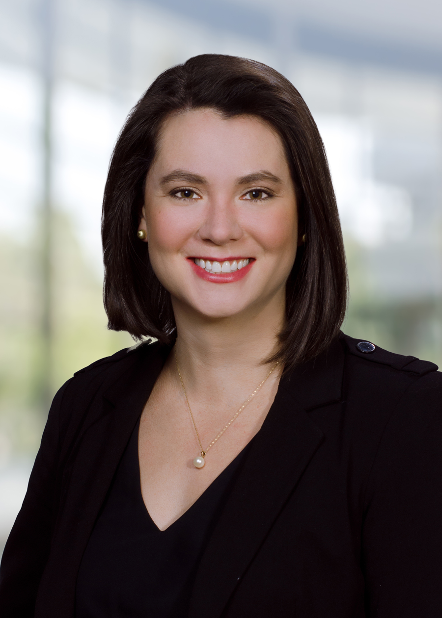 A woman wearing a black jacket and a necklace is smiling for the camera.