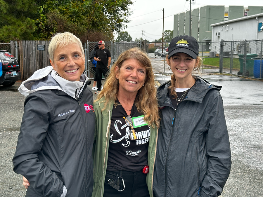 Three women are posing for a picture in a parking lot.