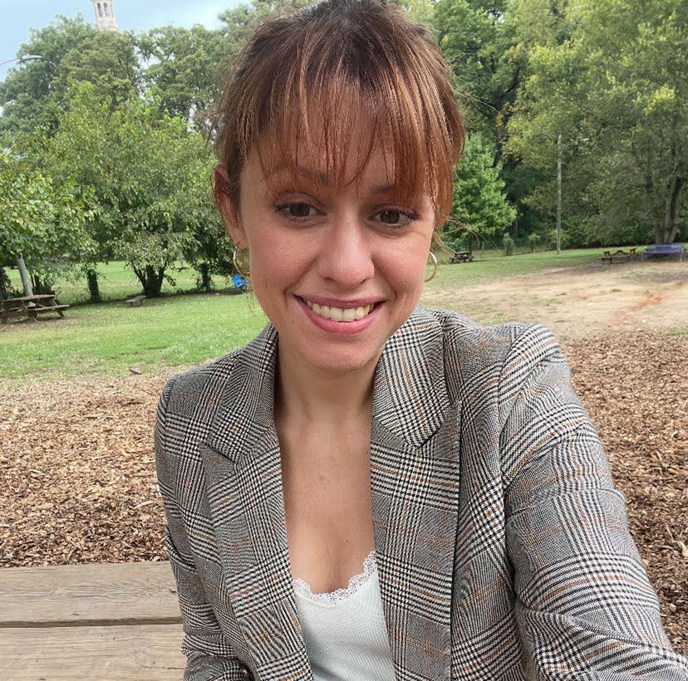 A woman with curly hair is wearing a white shirt and smiling.