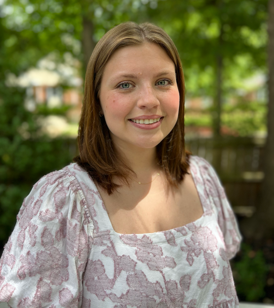A woman in a purple and white dress is smiling for the camera.