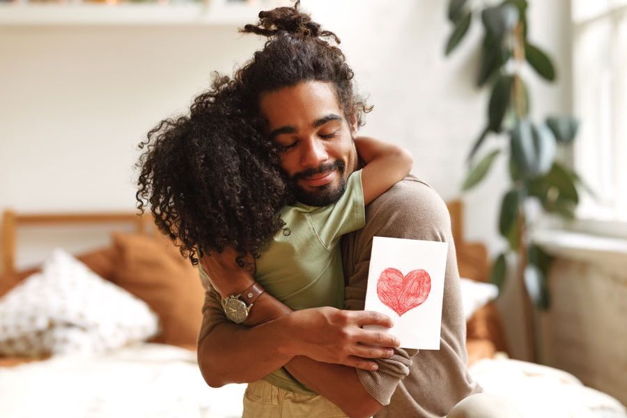 A man is hugging a woman who is holding a card with a heart on it.