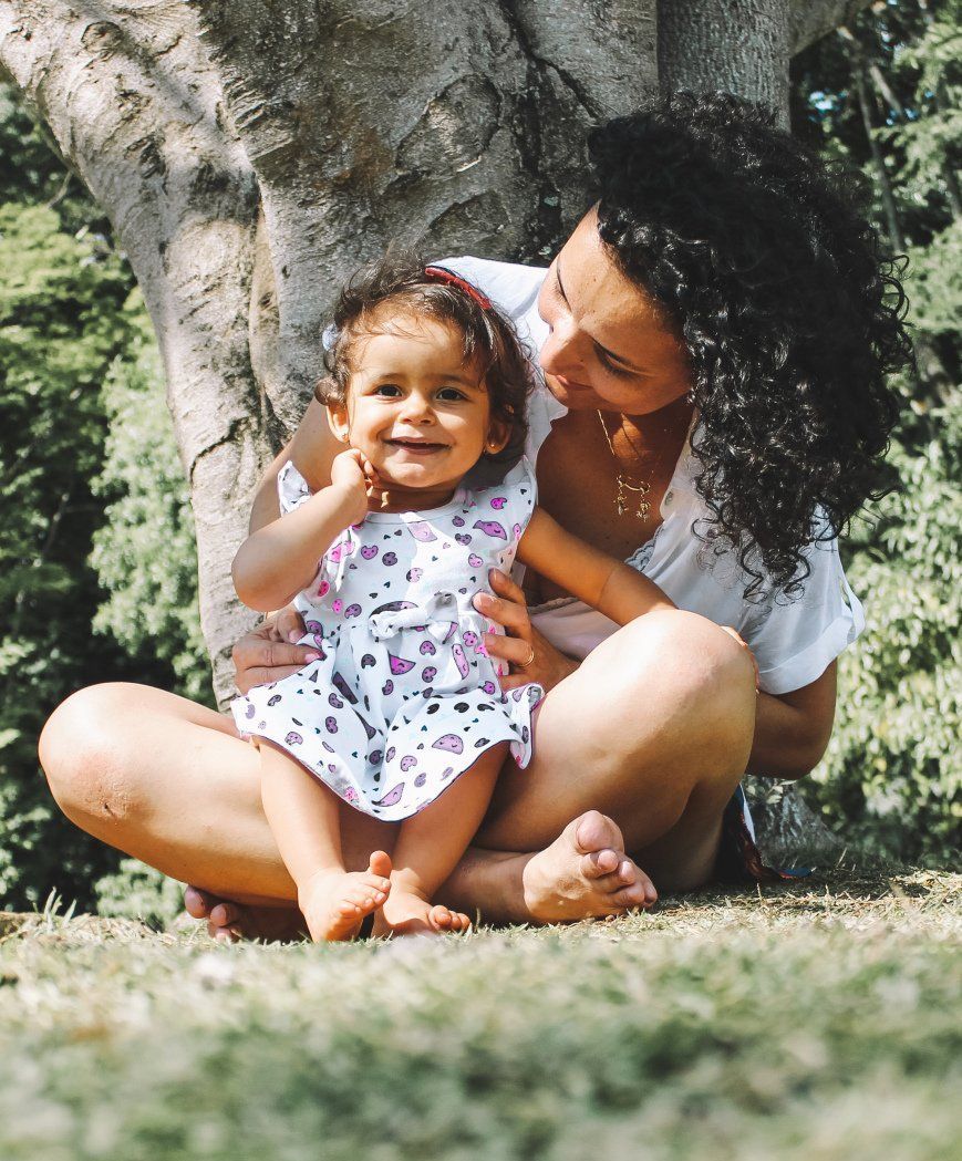 A woman is sitting on the grass holding a little girl.