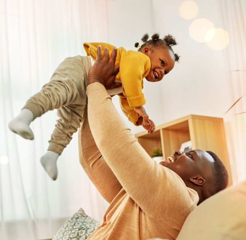 A man is holding a baby in the air while sitting on a couch.