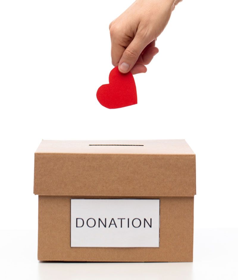 A hand is putting a red heart into a donation box