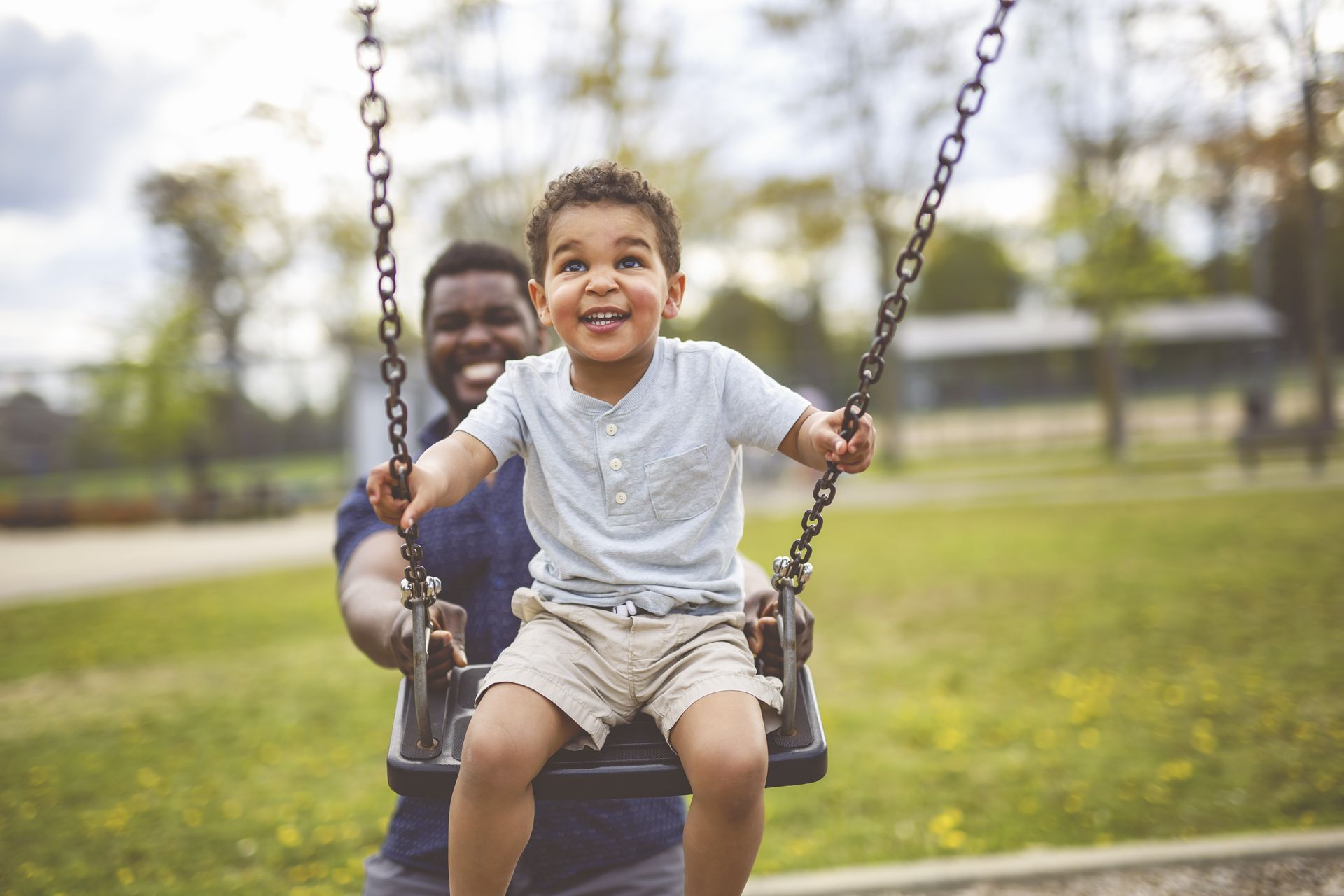 Little boy being swung on a swing by father in a park 