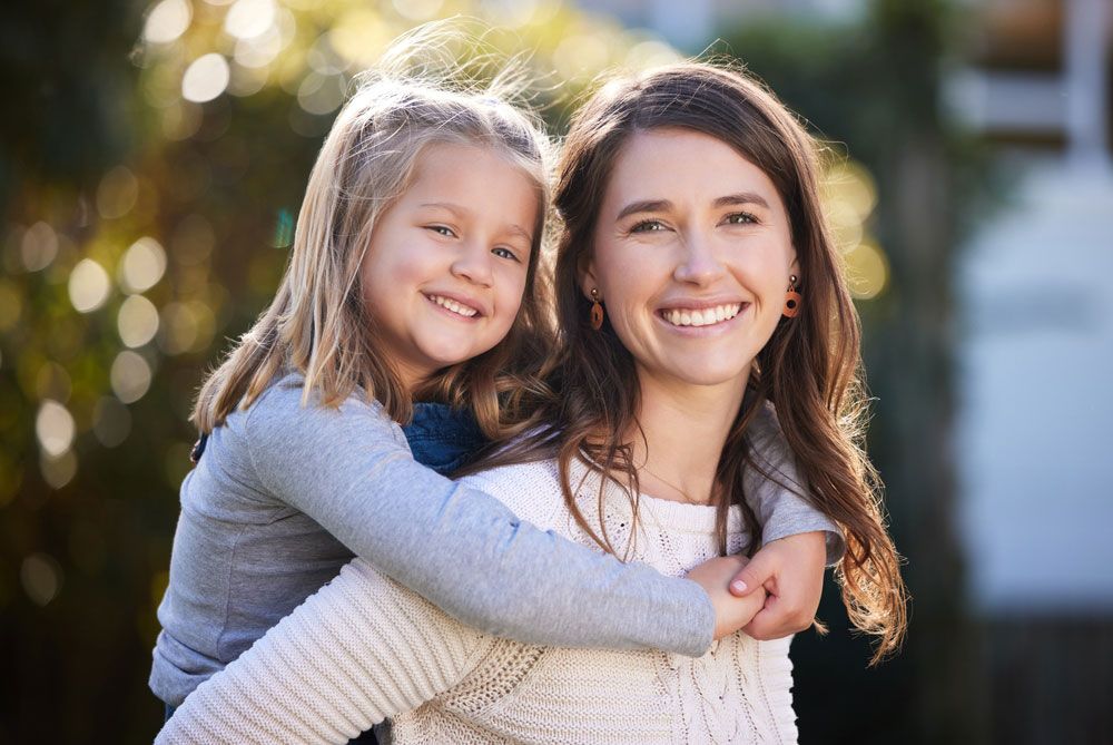 A woman is carrying a little girl on her back.