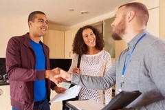a man and woman are shaking hands with a real estate agent in a kitchen .