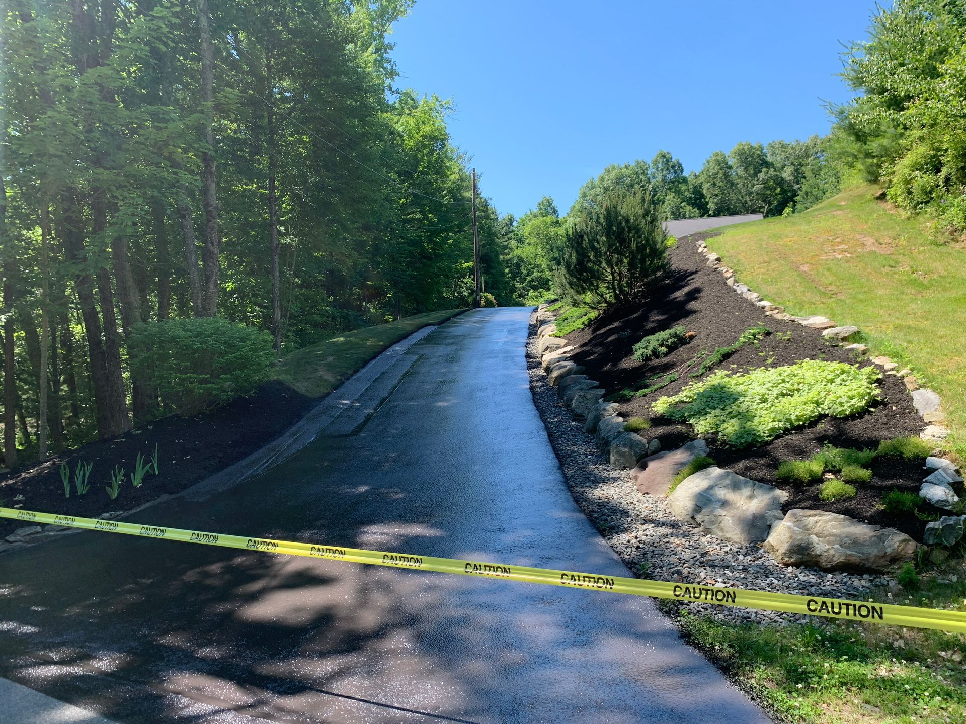 Newly paved driveway with landscaping and caution tape.