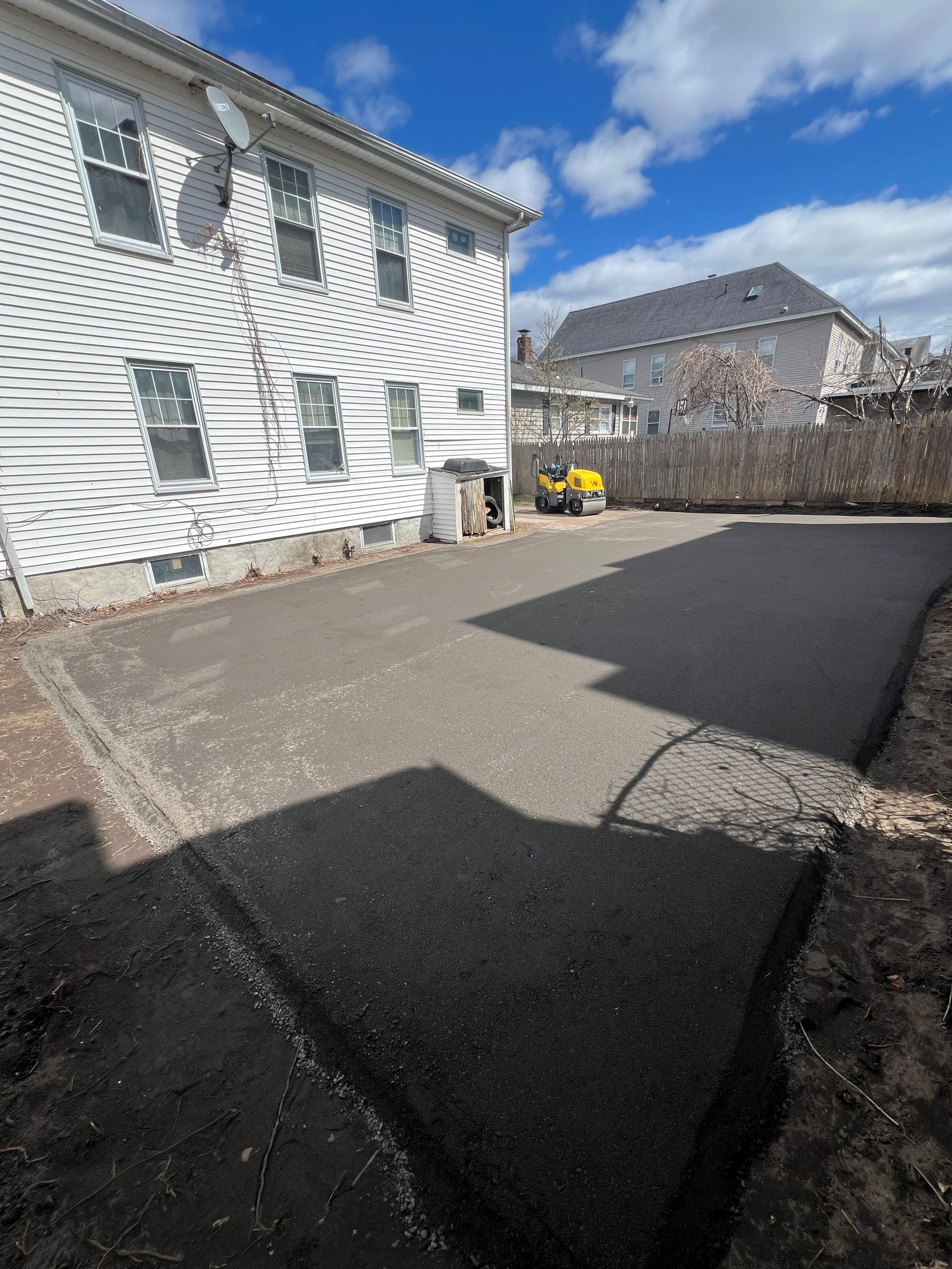 Newly paved asphalt driveway next to a white building; blue sky overhead.