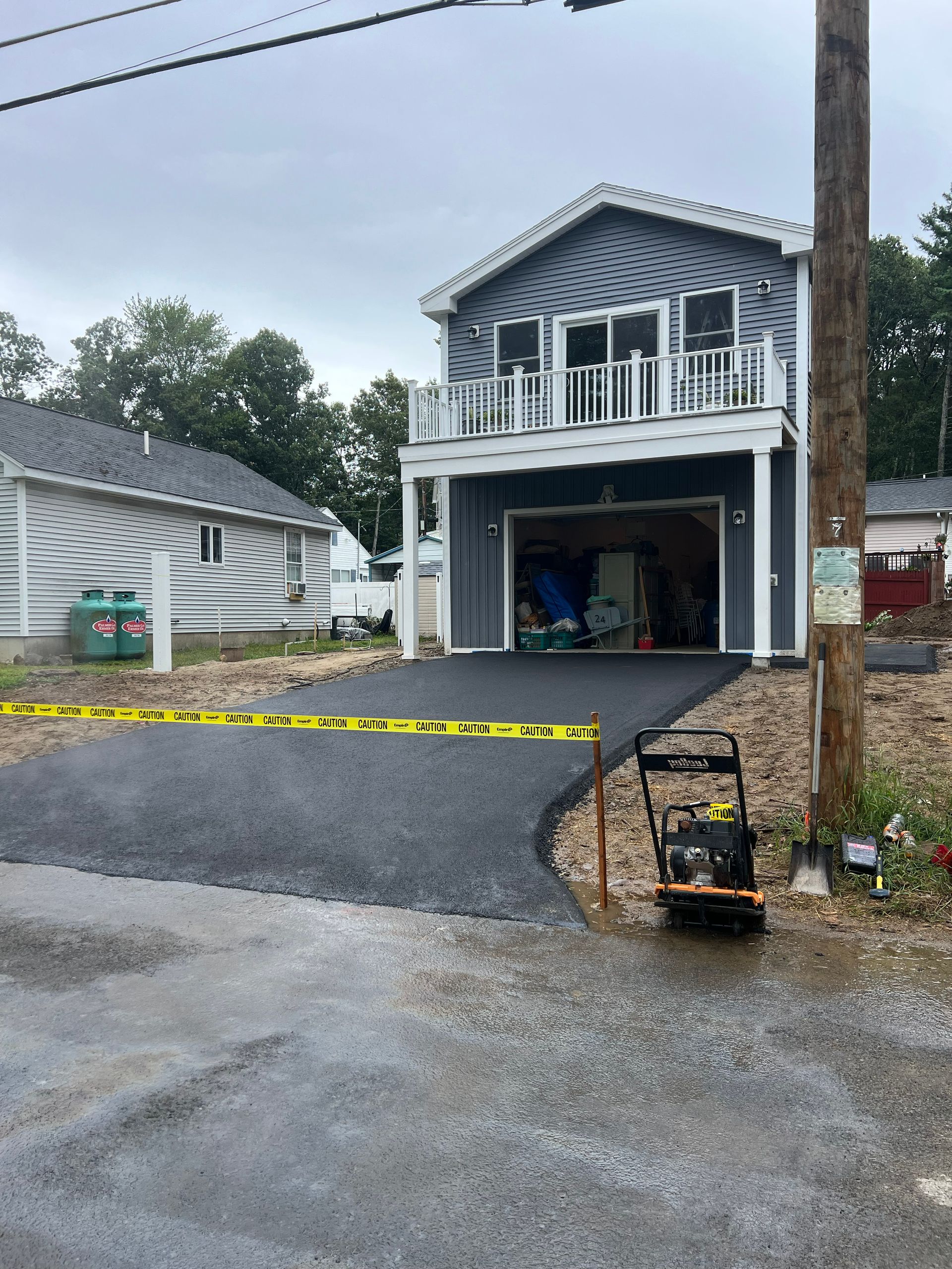 New asphalt driveway leading to a two-story blue house with an open garage.
