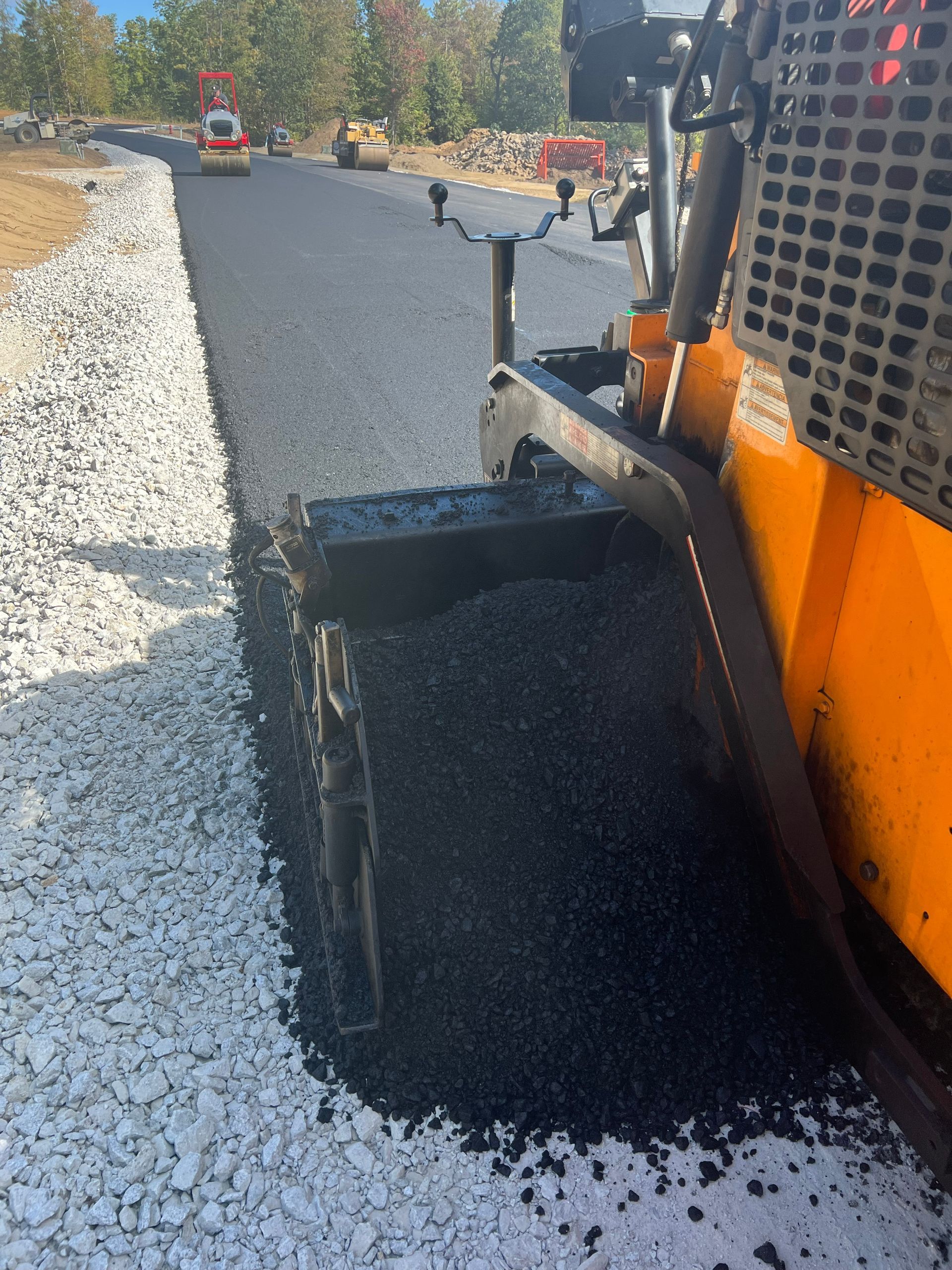 An asphalt paving machine laying blacktop on a road beside a gravel border.