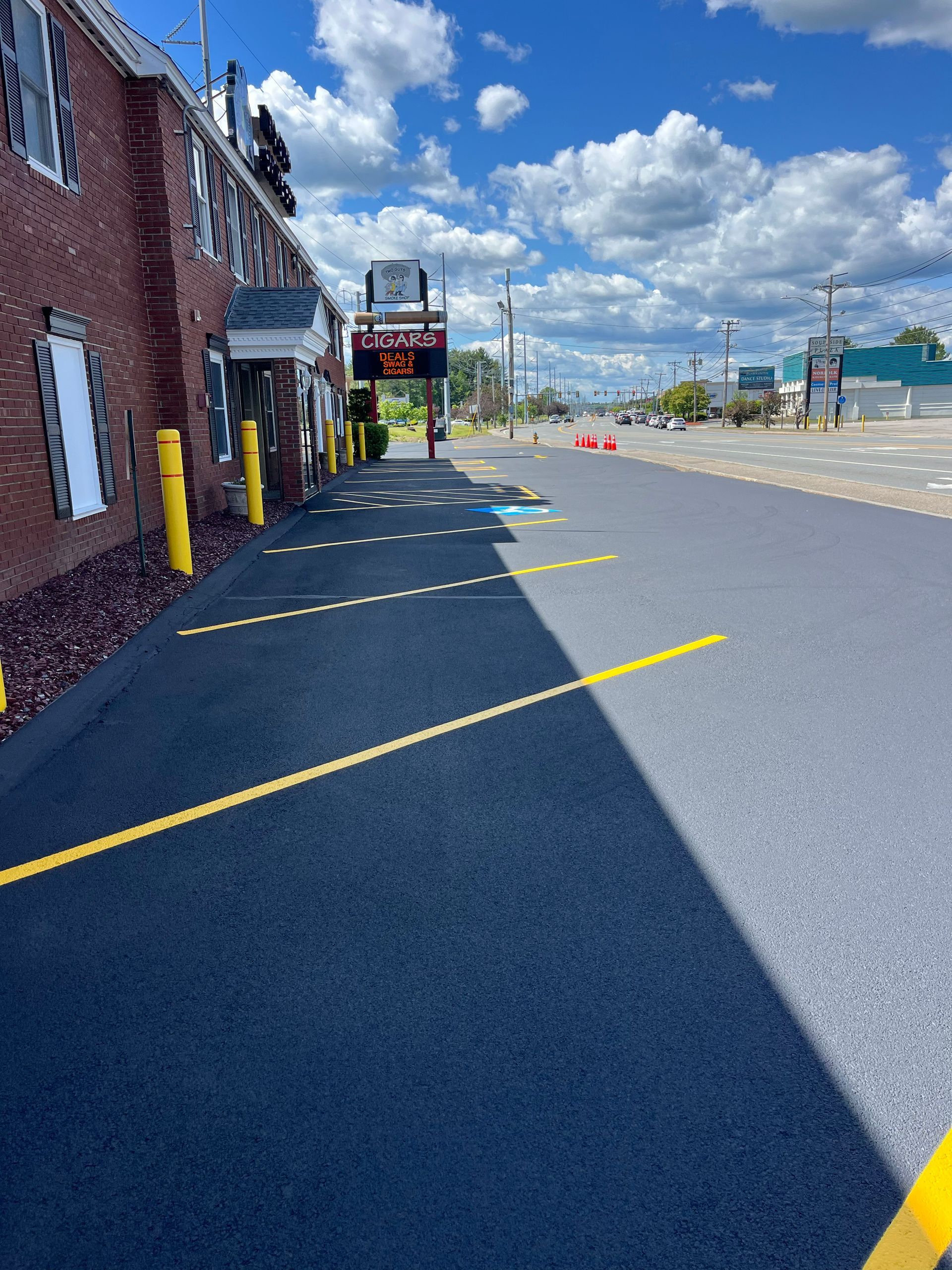 Exterior of building with new asphalt parking lot; yellow parking lines and bumpers. Sunny day.