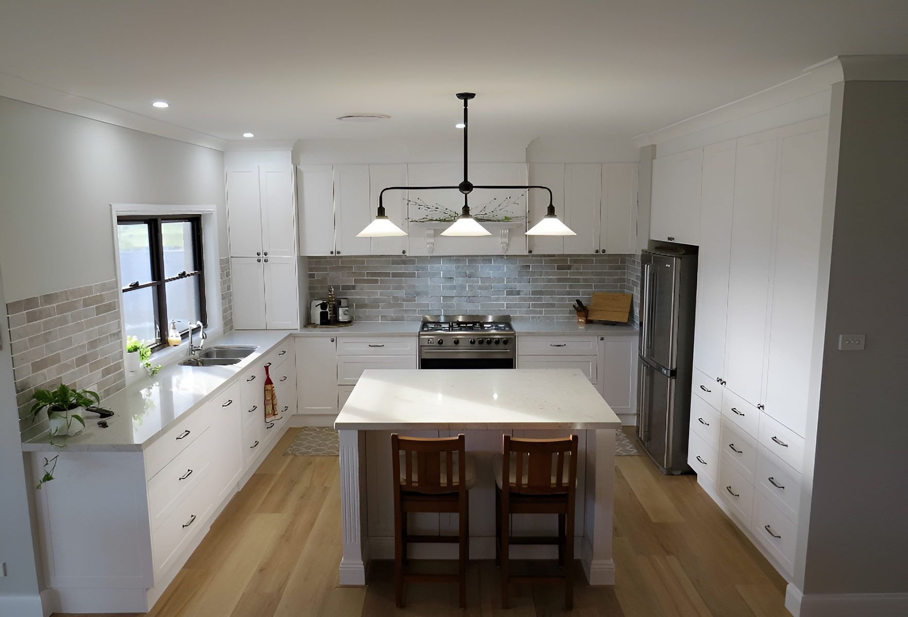 Modern Kitchen With a Central Island With Two Wooden Chairs — Piscopo Kitchens Plus In Smiths Lake, NSW