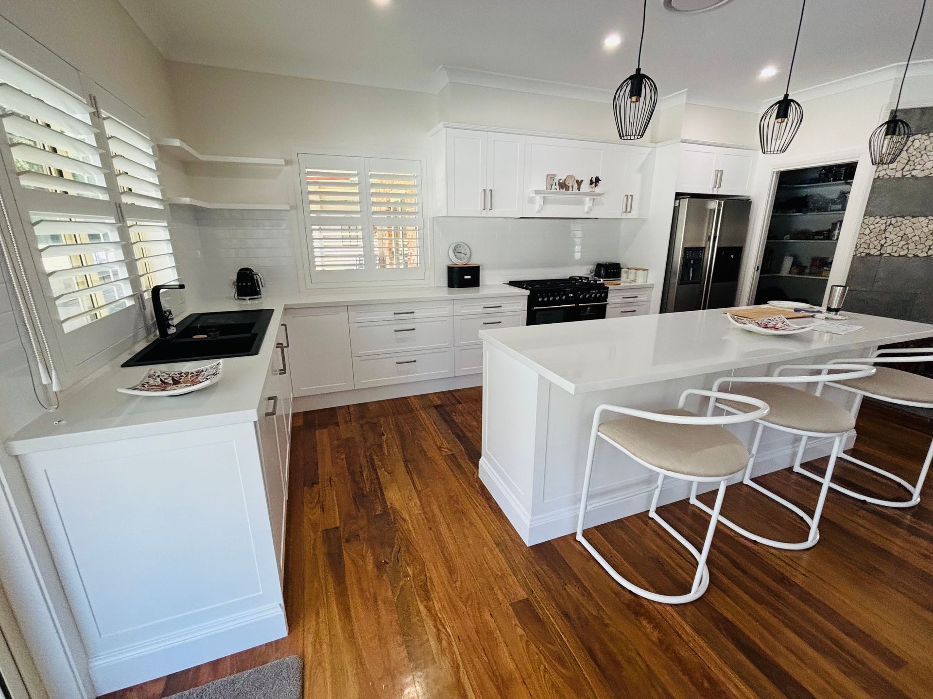 White kitchen with wooden floors, island with seating, white cabinets, and stainless steel appliances. — Piscopo Kitchens Plus In Forster, NSW
