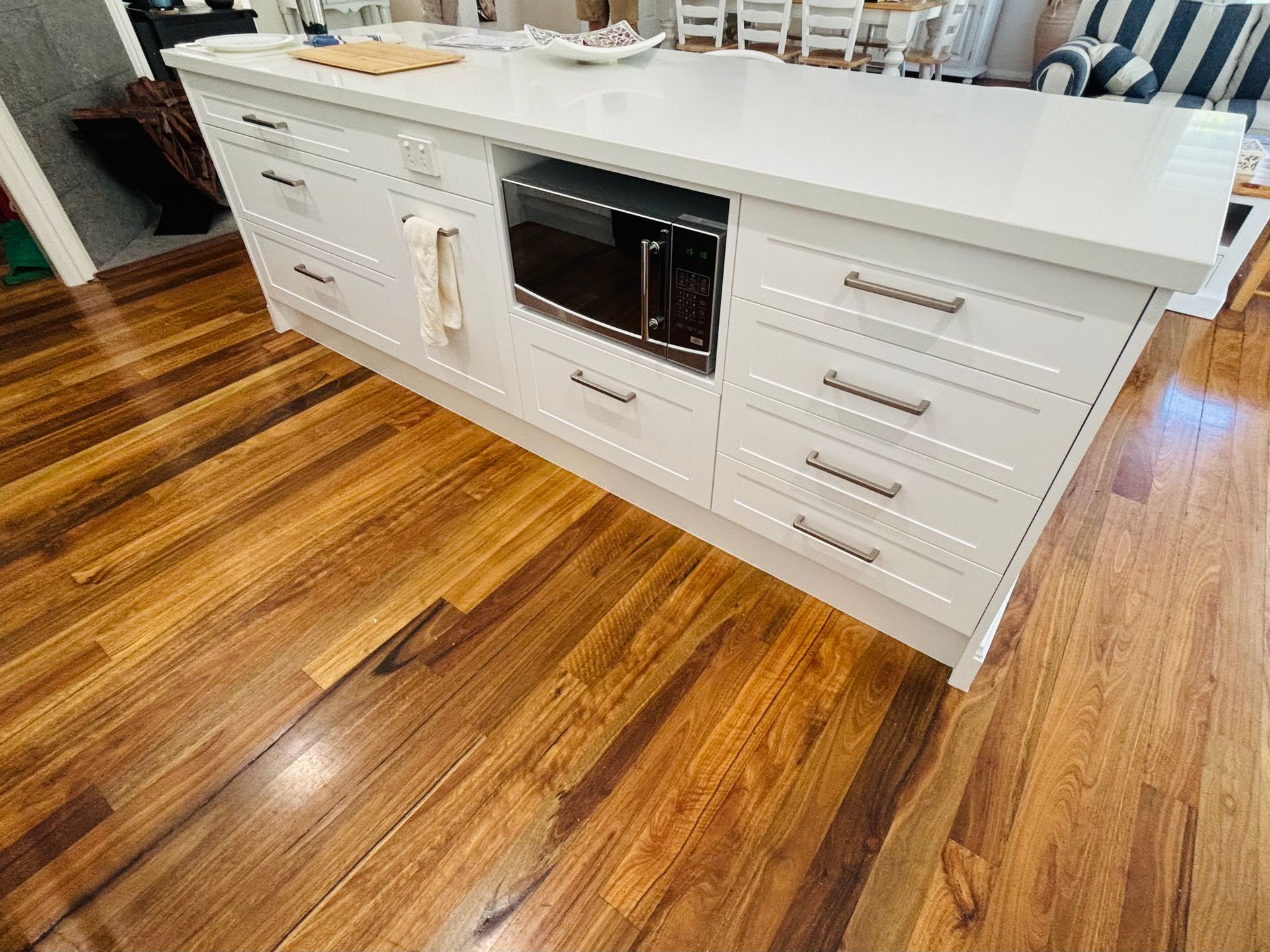 Kitchen island with white cabinets, built-in microwave, and hardwood floor. — Piscopo Kitchens Plus In Forster, NSW
