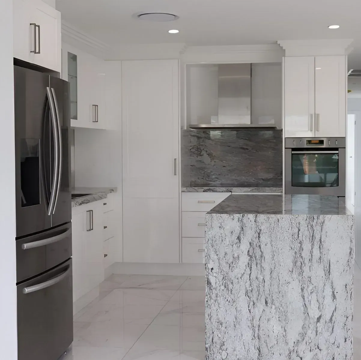 White kitchen with stainless steel appliances, granite countertops, and an island. Piscopo Kitchens Plus In Forster, NSW