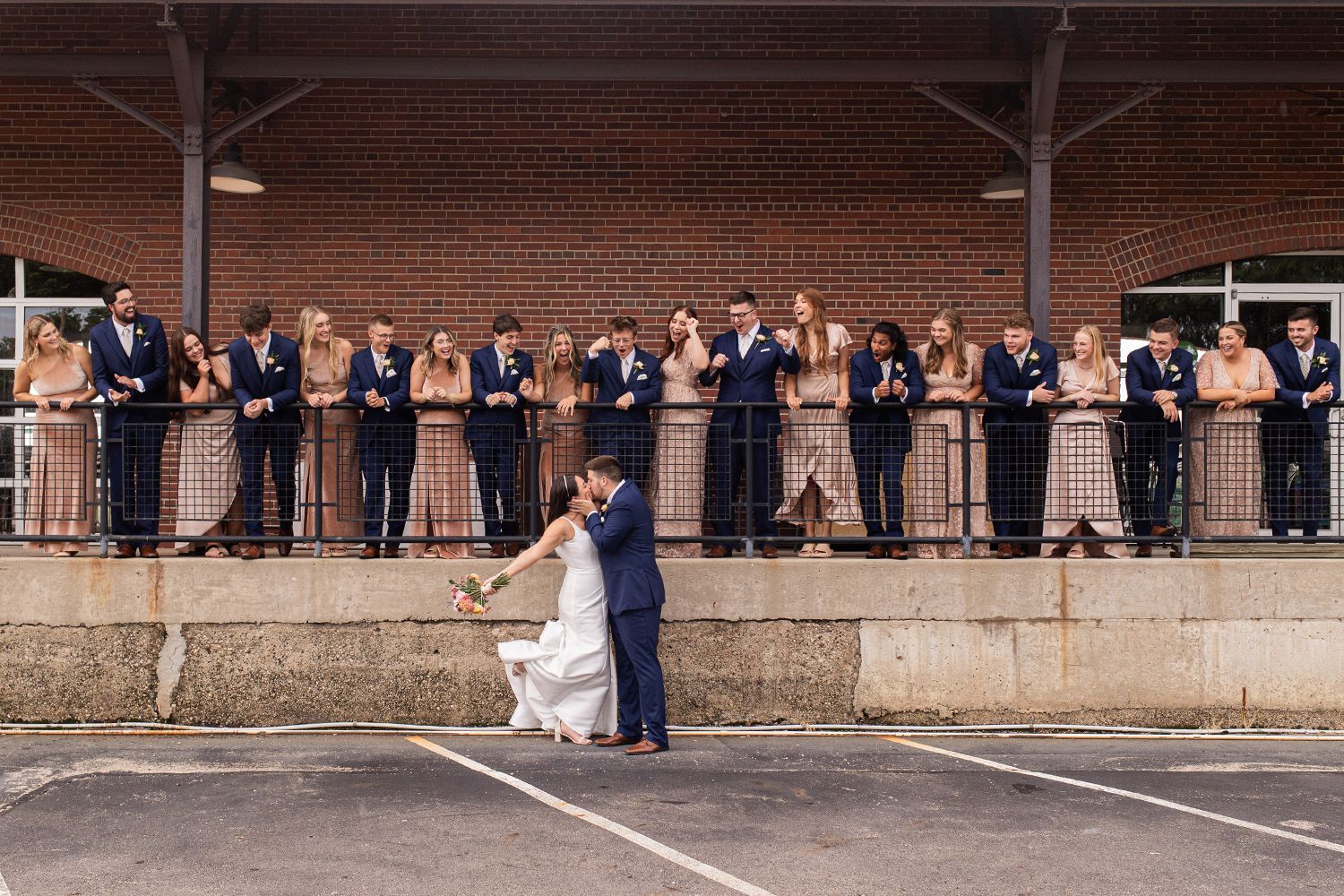 bride and groom kissing while wedding party watches from venue porch