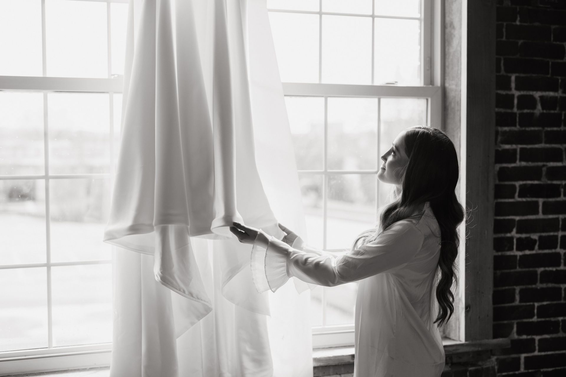 bride looking at gown hanging in window