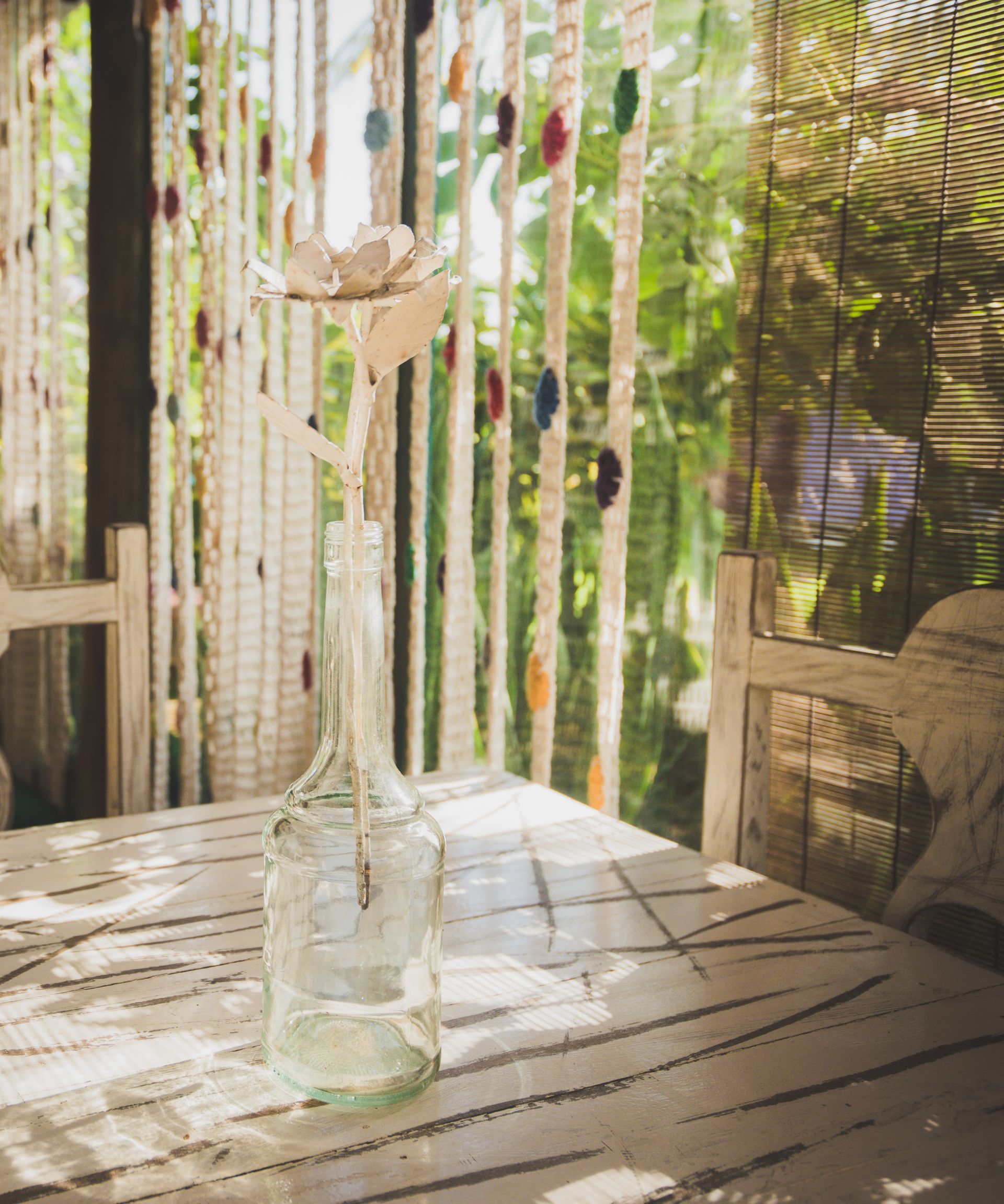 Um vaso com uma flor dentro está sobre uma mesa em frente a uma janela.