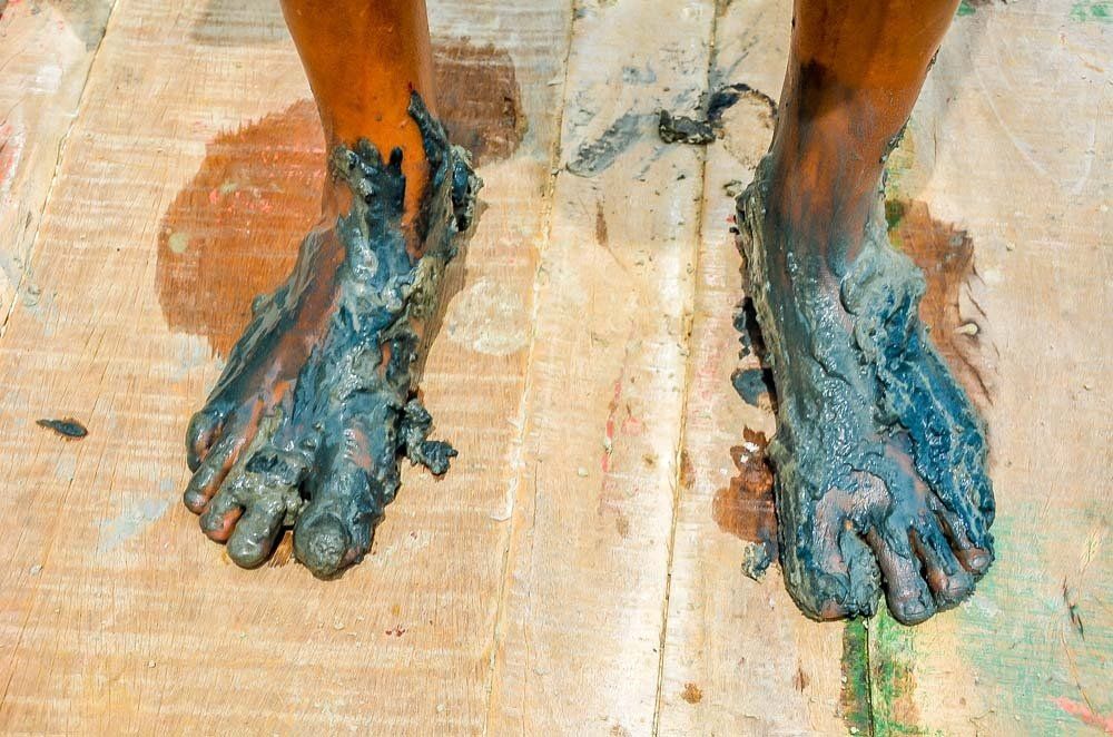 Os pés de uma pessoa estão cobertos de lama em um piso de madeira.