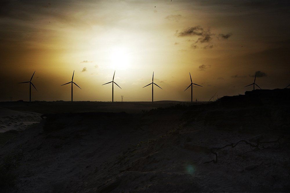 Uma fileira de turbinas eólicas se destaca contra o céu do pôr do sol.