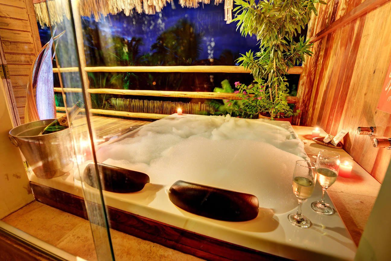 Há uma jacuzzi no meio da sala com duas taças de vinho.