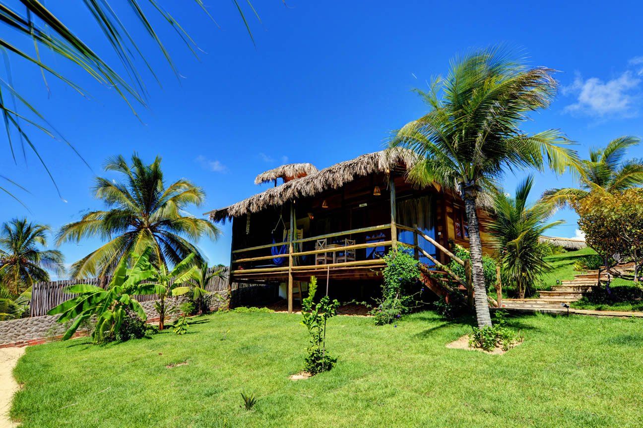 Uma pequena casa de madeira com telhado de palha cercada por palmeiras.