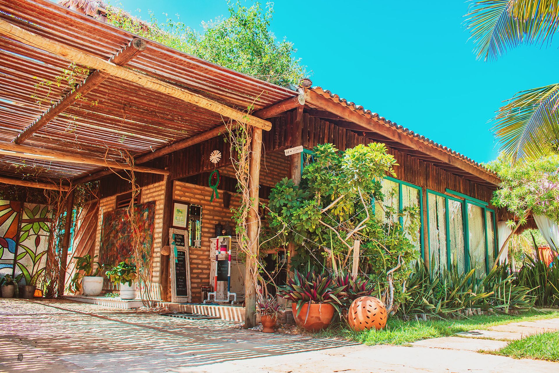 Uma casa com telhado de madeira e uma varanda de madeira cercada por árvores e plantas.