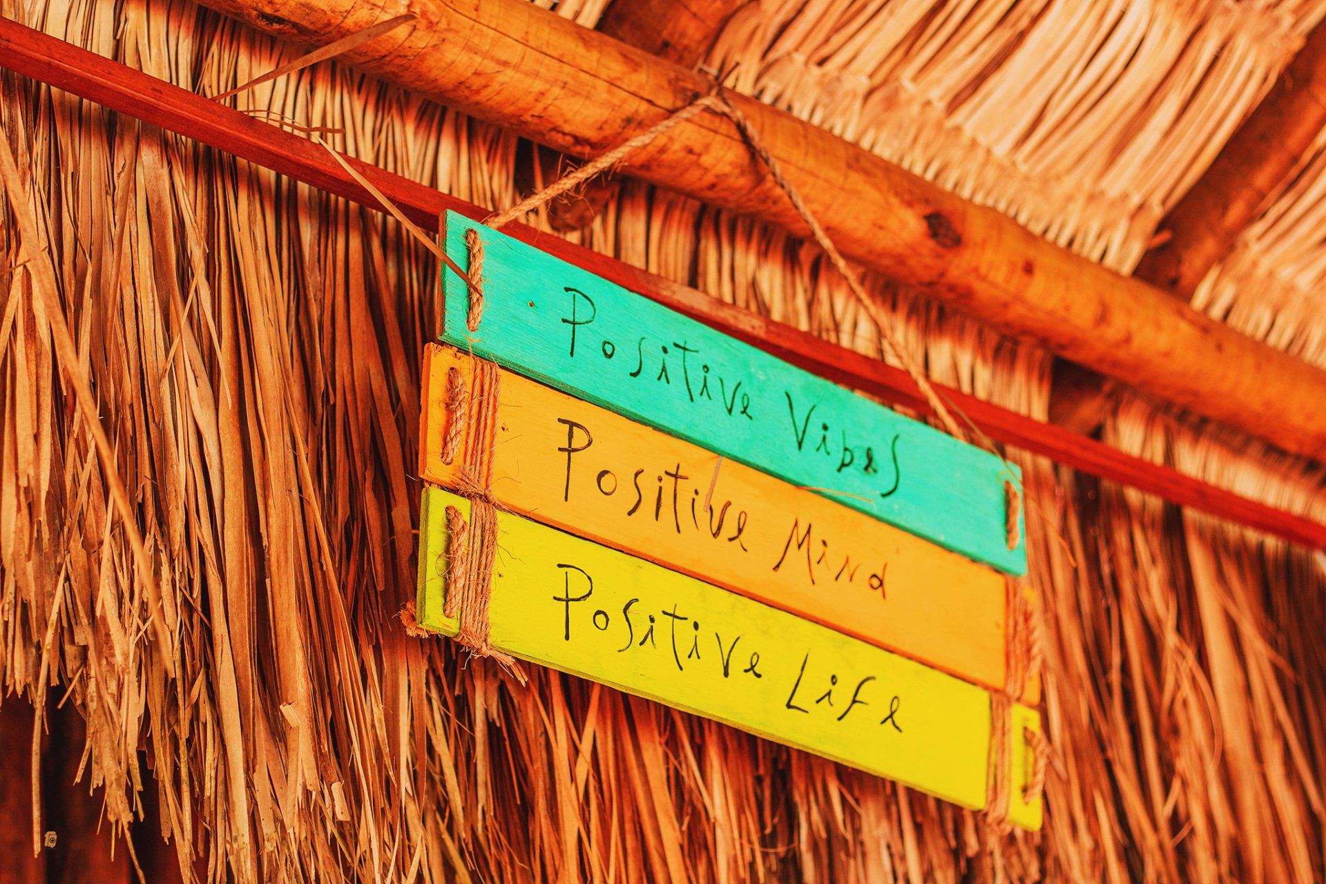 Uma placa que diz vibrações positivas, mente positiva, vida positiva está pendurada em um telhado de palha.