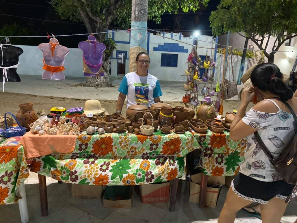 Uma mulher está tirando uma foto de um homem atrás de uma mesa cheia de potes de barro
