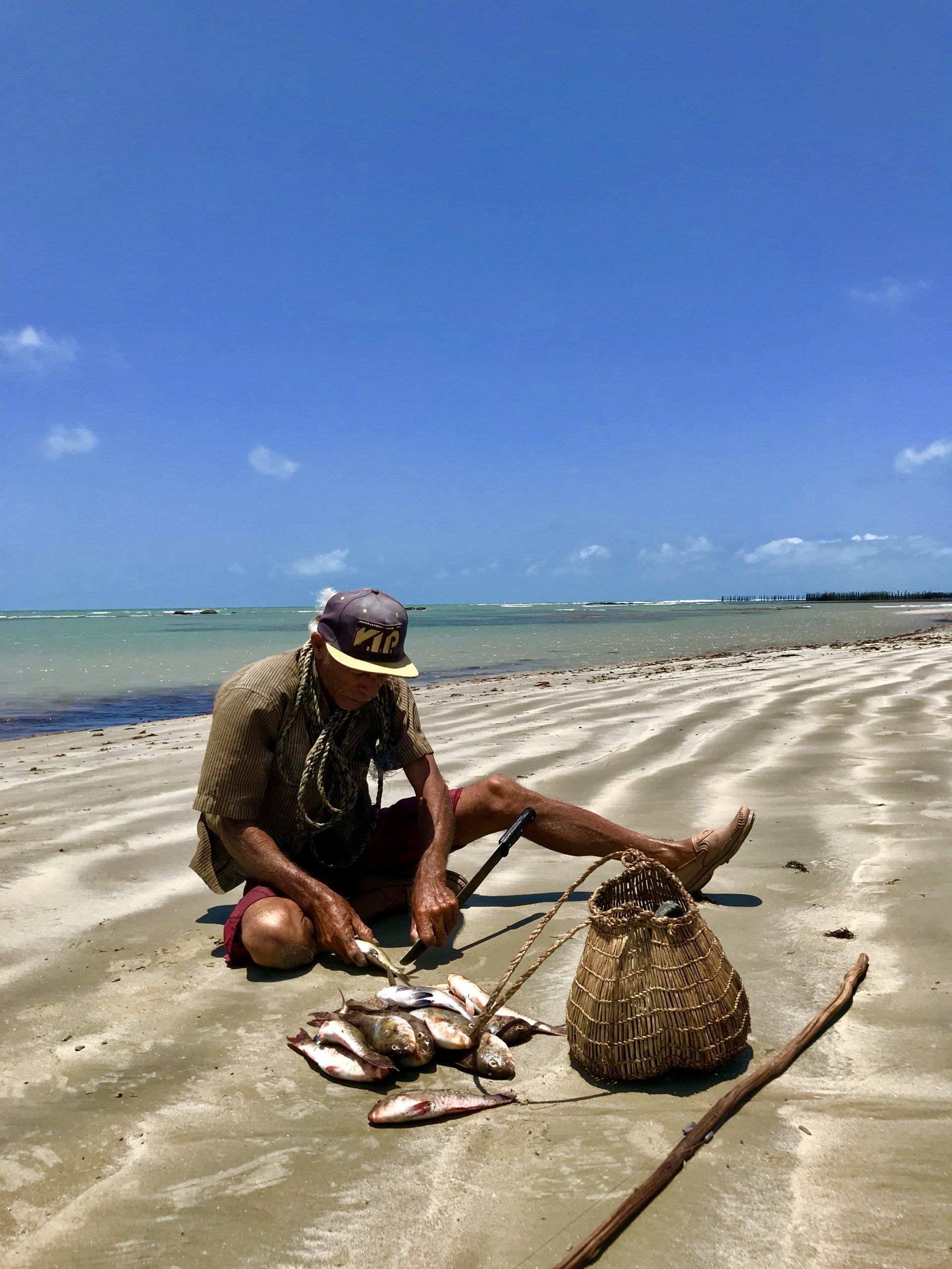 Um homem está sentado na praia com um saco de peixes.
