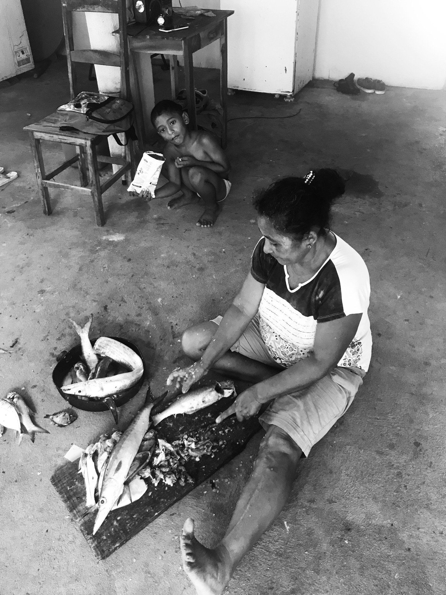 Uma mulher está sentada no chão cortando peixe em uma tábua de corte.